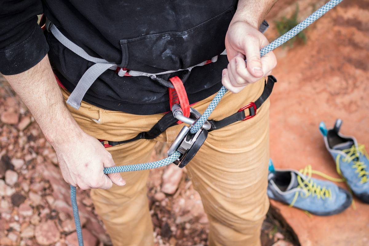 Close-up of certified climbing carabiner with visible CE and UIAA markings next to frayed, uncertified sling illustrating climbing safety standards